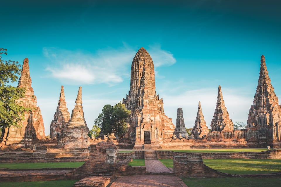 Ancient stone structures with multiple spires, surrounded by greenery and a clear sky.
