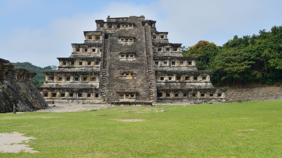 A large stone pyramid with multiple levels and a surrounding grassy area.
