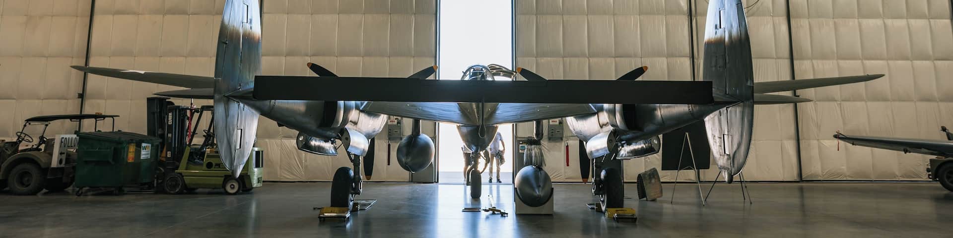 A large aircraft inside a hangar with a tractor and a forklift.