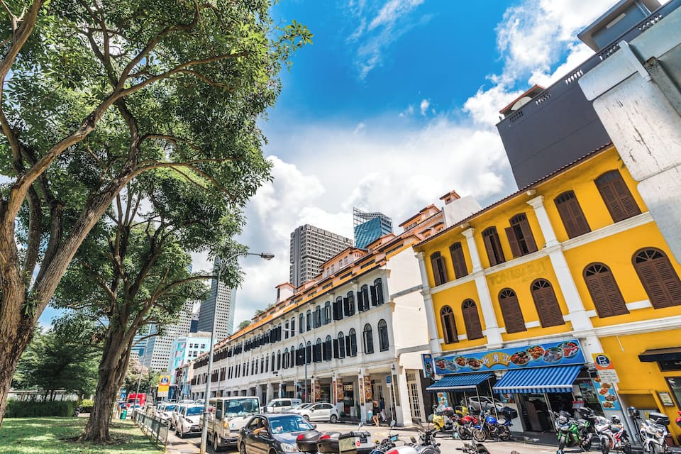 A street lined with historic buildings, trees, and parked vehicles.
