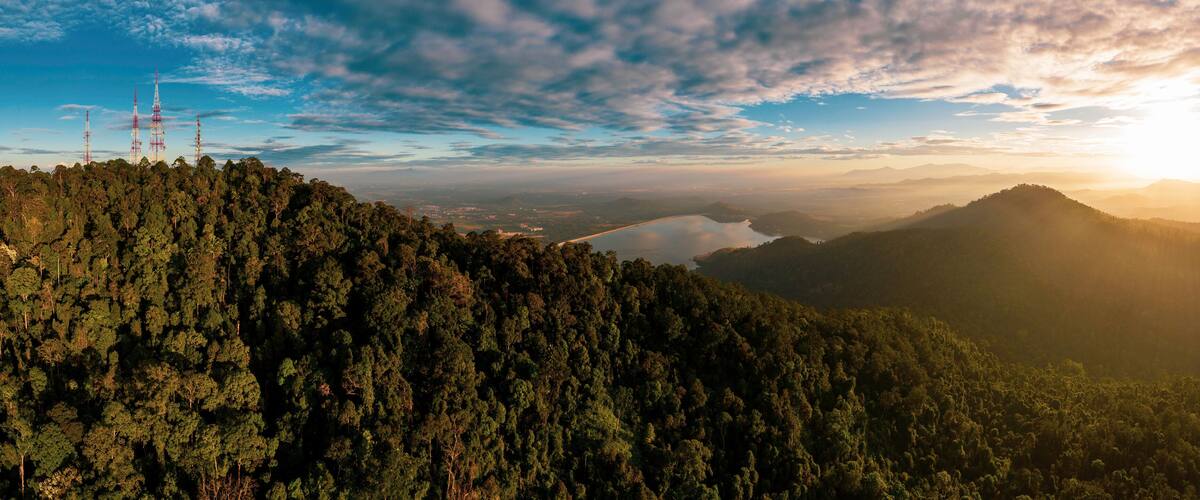 A dense forested mountain range with a lake and distant cityscape.