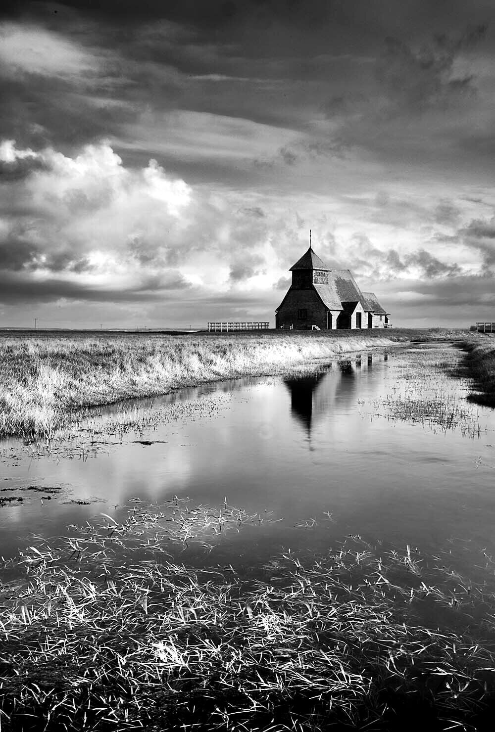 Paisaje en blanco y negro con una iglesia y un muelle que se adentra en el agua.