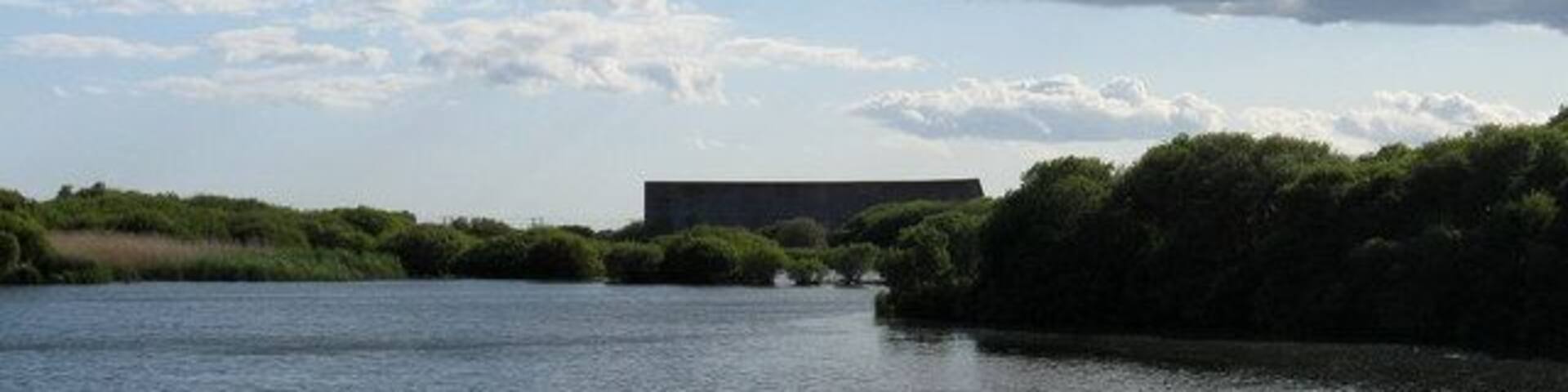 Sound Mirror View across a water filled gravel pit to the largest of the three sound mirrors built between 1927-30. Designed to detect low flying aircraft across the channel they were made obsolete by the invention of radar. The gravel pits came later and for a while threatened the existence of these concrete mirrors but the monuments were saved in 2003.