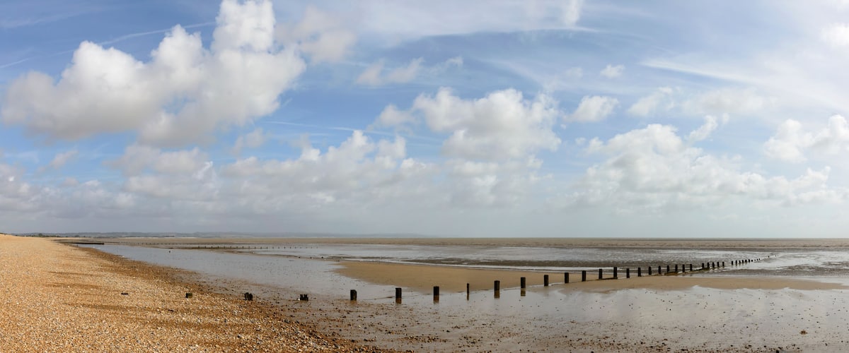 A beach with pebbles, a wooden jetty, and a cloudy sky.