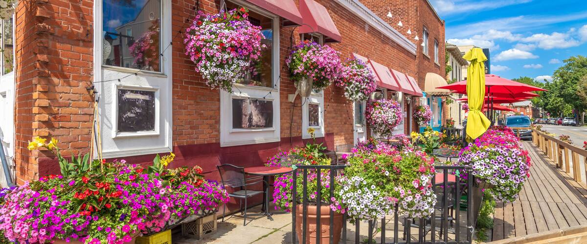 A brick building with red awnings, hanging flower baskets, and outdoor seating.