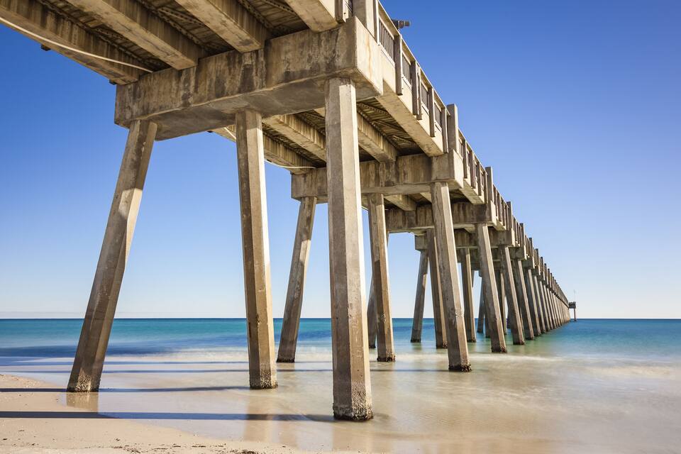 A long pier extending into the ocean with clear blue water and a sandy beach.
