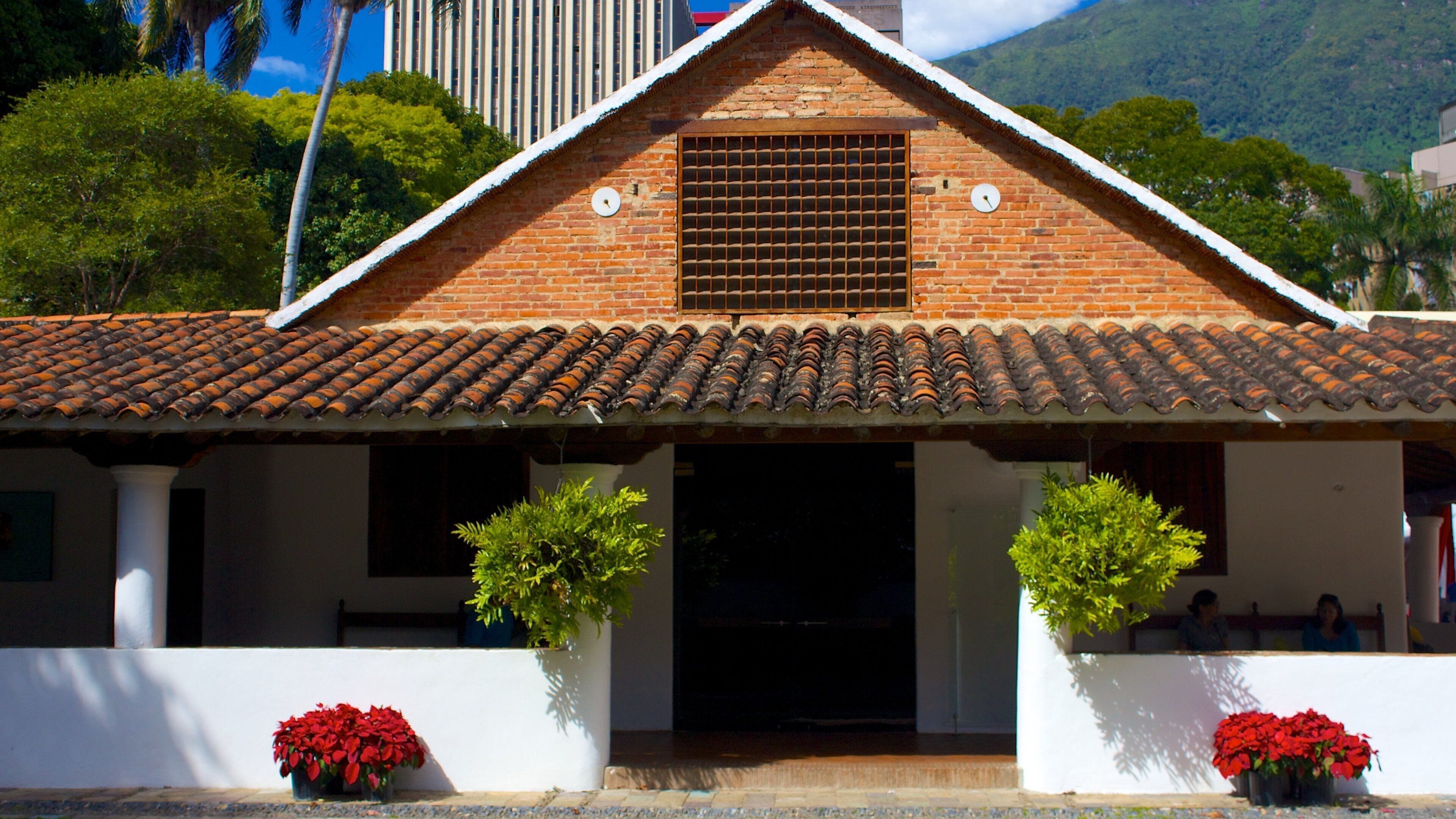 A traditional brick building with a tiled roof, two potted plants, and red flowers in front.