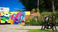 A colorful mural, a paved walkway, and a wooden bench in a park.