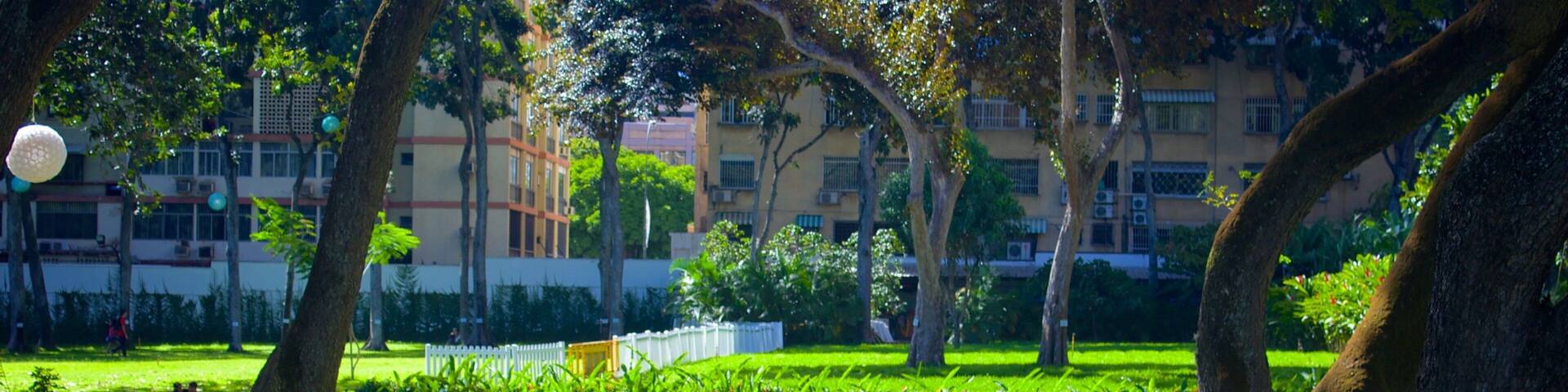 A well-maintained park with manicured lawns, geometric flower beds, and mature trees.