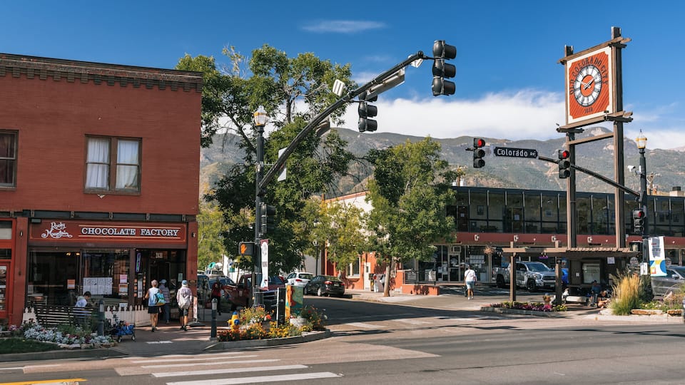 A street corner with a clock, a traffic light, and a building labeled 'Rocky Mountain Chocolate Factory.'