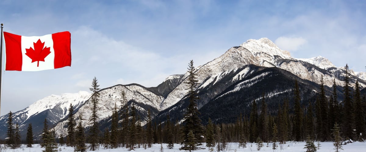 A Canadian flag, snow-covered mountains, and coniferous trees.