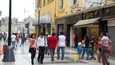 A busy urban street with pedestrians, a yellow building, and a storefront with a sign reading "Cesar."
