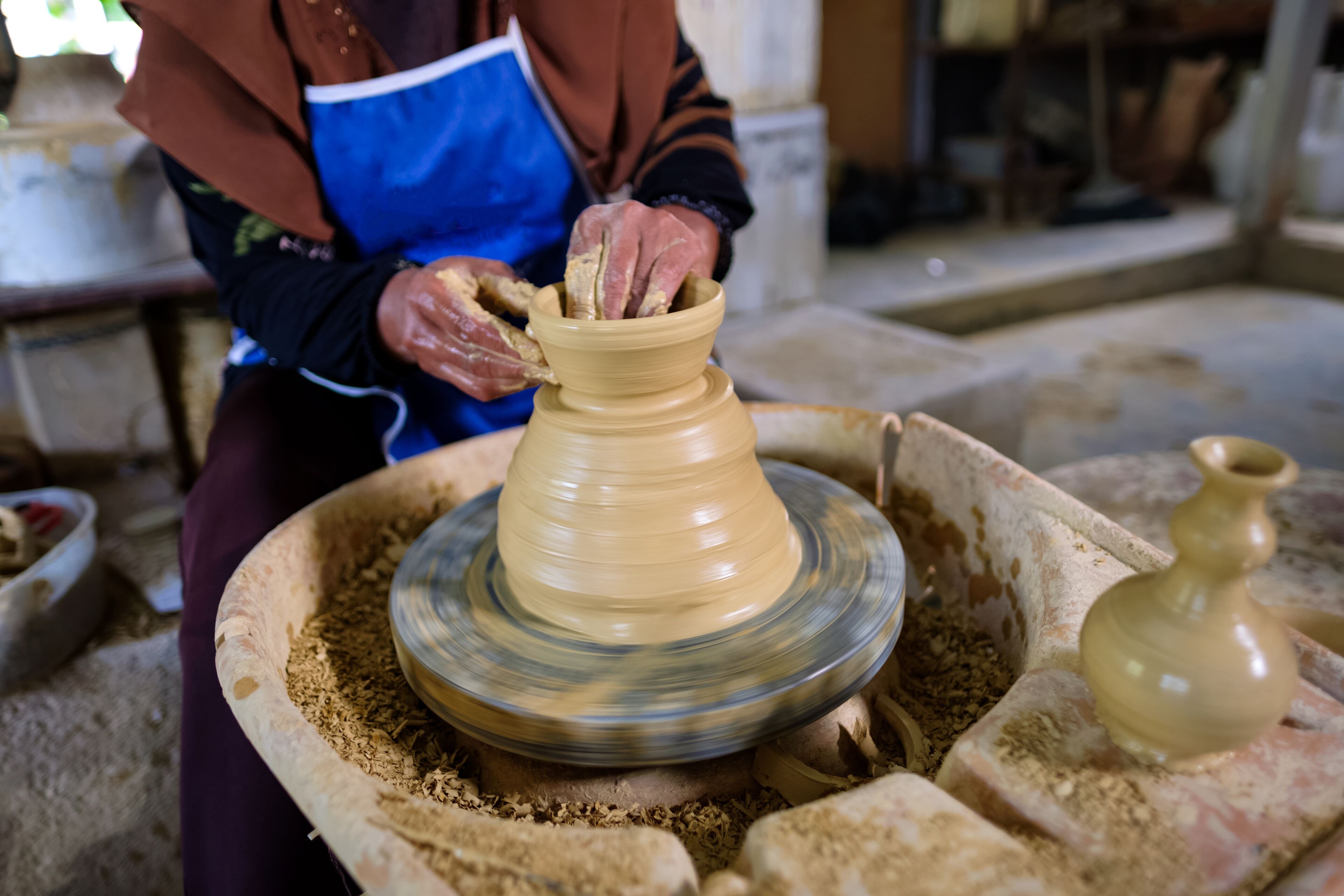 A person shaping a clay pot on a pottery wheel.