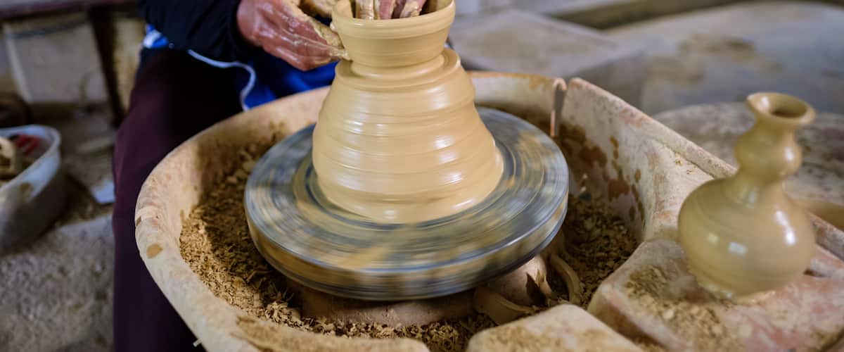 A person shaping a clay pot on a pottery wheel.