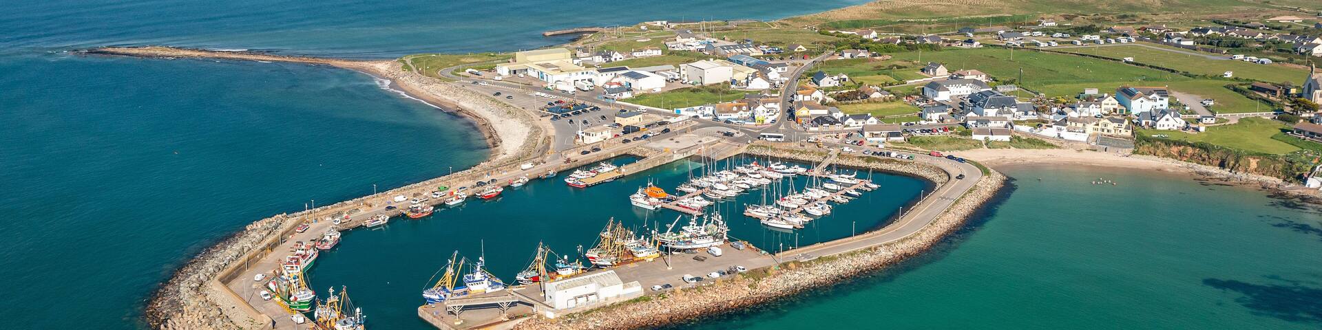 An aerial view of a coastal town with a marina, harbor, and surrounding landscape.