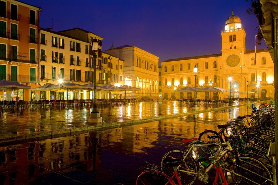 A nighttime view of a canal with buildings and a clock tower reflecting on the water.