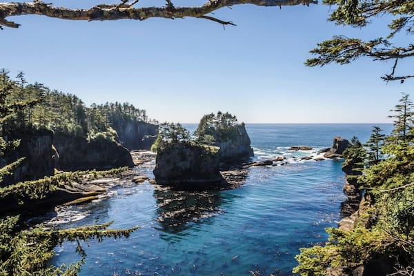 A coastal landscape with rocky cliffs, clear blue water, and dense green forests.
