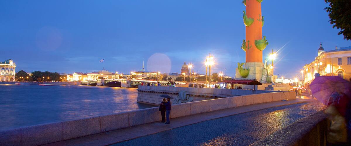 A tall, colorful tower with green and orange sections, surrounded by water and city buildings at dusk.