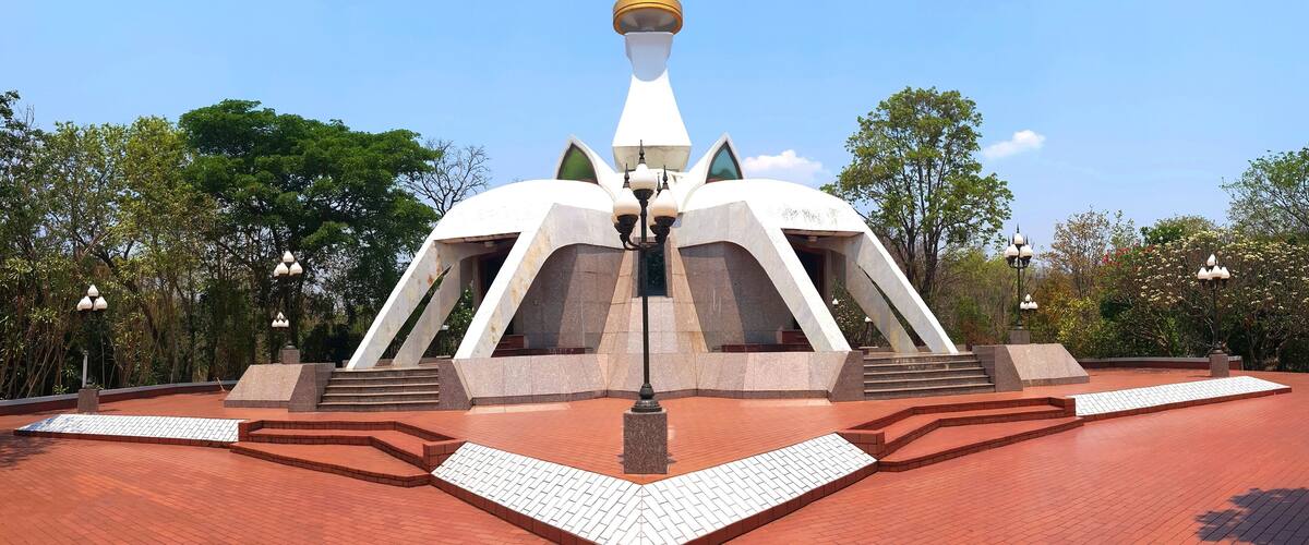 A modern architectural structure with a white and gold spire, surrounded by a red brick plaza and greenery.