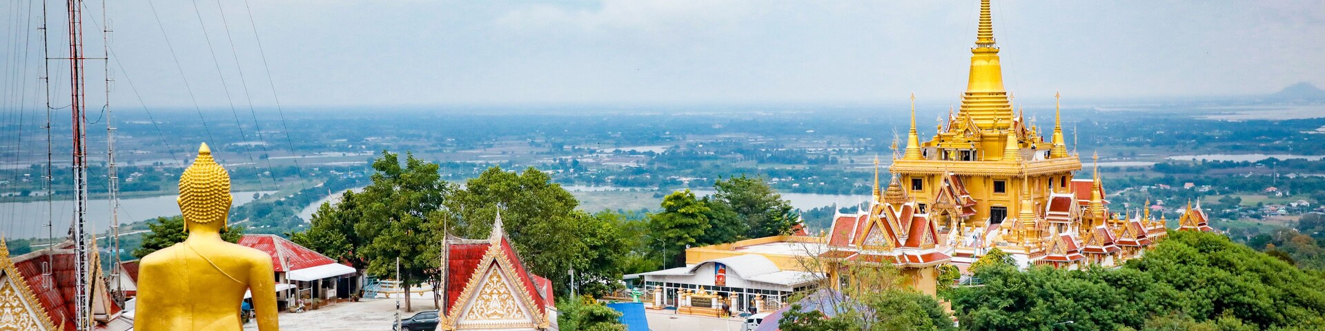 Uma grande estátua dourada de Buda, um stupa dourado e um complexo de templos com telhados vermelhos.