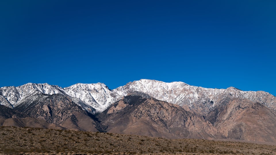 A mountain range with snow-capped peaks under a clear blue sky.