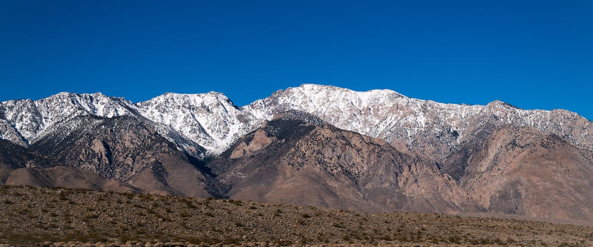 A mountain range with snow-capped peaks under a clear blue sky.