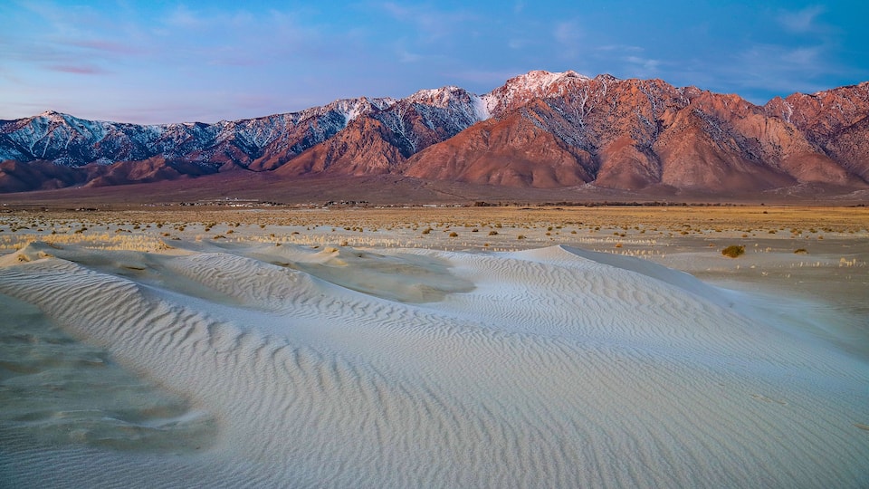 A desert landscape with sand dunes and snow-capped mountains in the background.