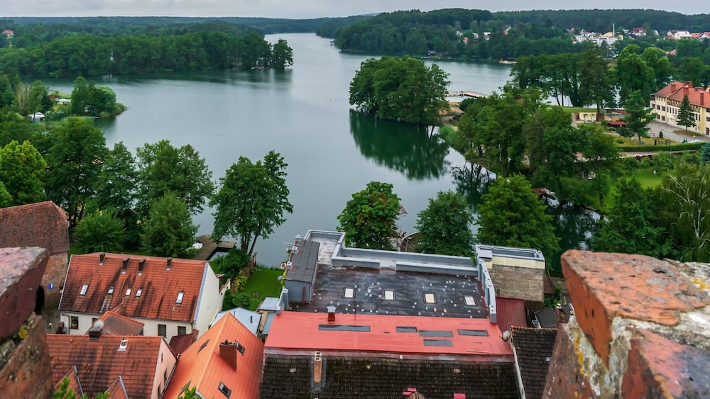 Une rivière bordée de forêts denses et une ville aux bâtiments aux toits rouges.