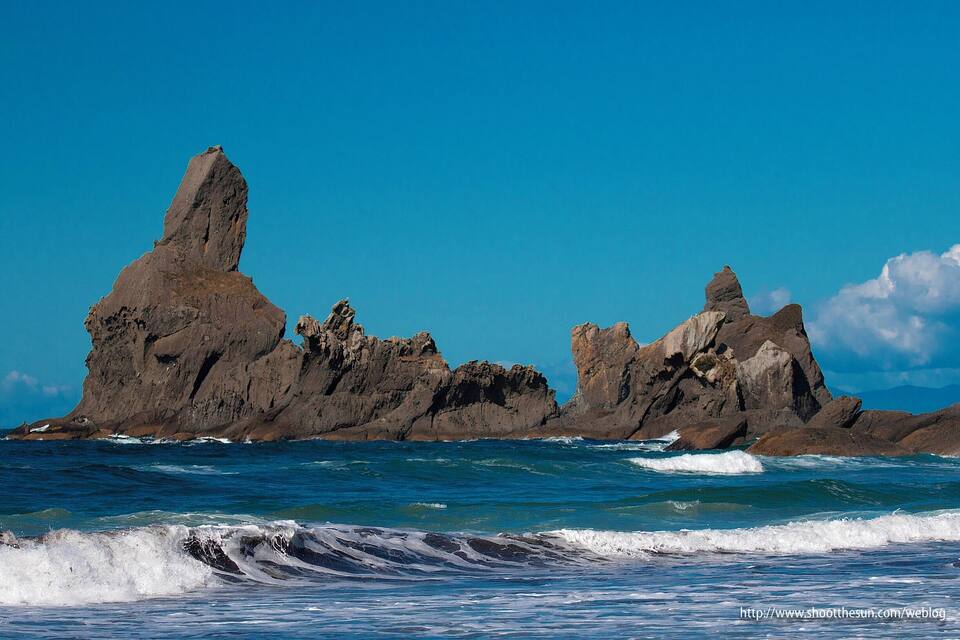 A rocky coastline with prominent rock formations and waves crashing against them.