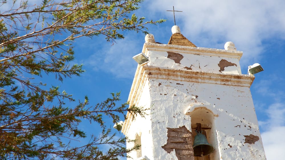 A weathered bell tower with a cross on top, surrounded by trees.