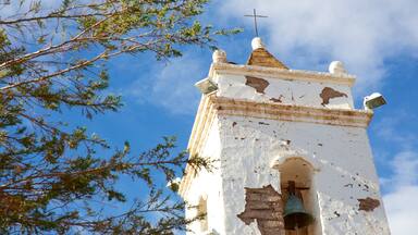 Um campanário desgastado com uma cruz no topo, rodeado de árvores.