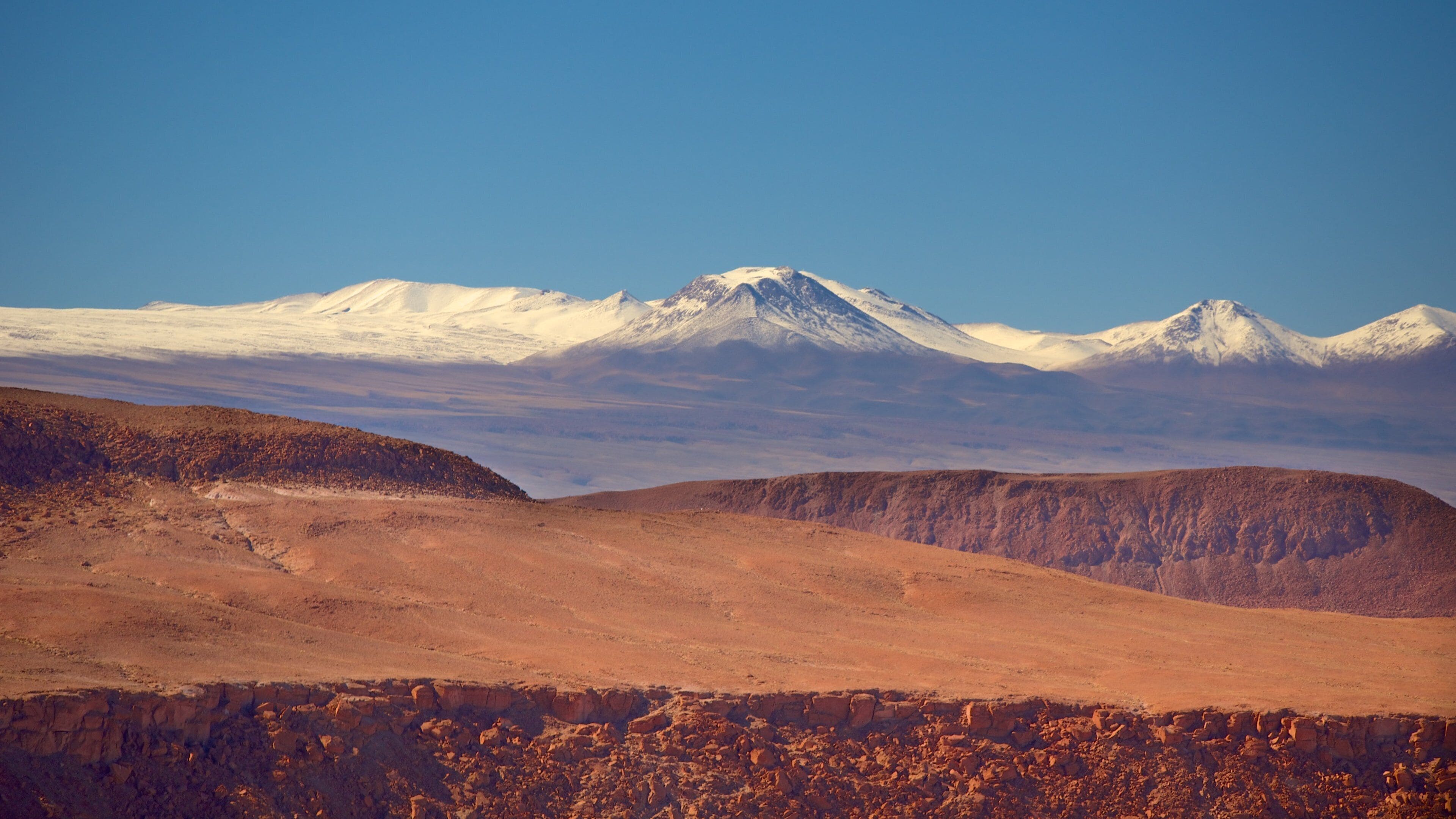 A mountainous landscape with snow-capped peaks and a barren foreground.