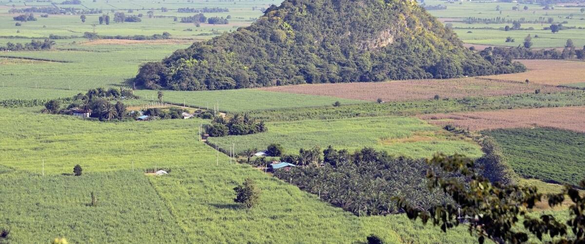 A lush green landscape with a prominent hill in the center, surrounded by fields and distant mountains.