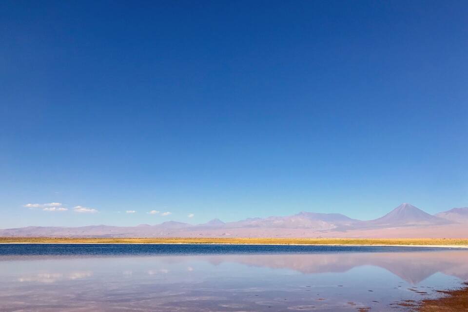 Un lago tranquilo con el reflejo nítido del cielo y montañas al fondo.