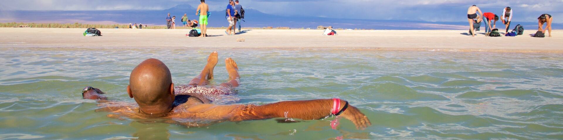 A person swimming in the ocean with a beach and people in the background.