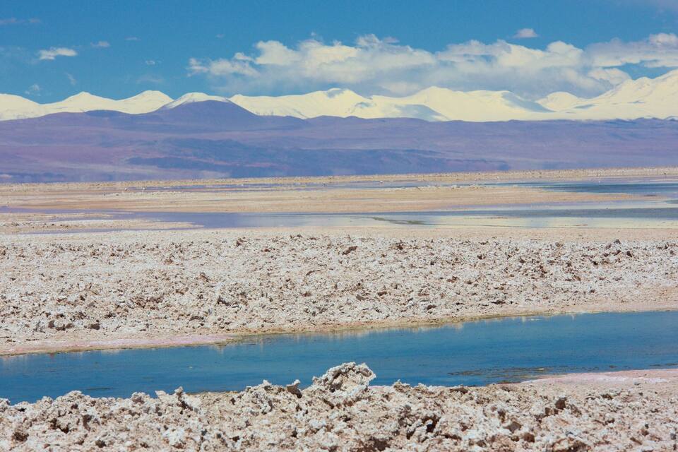 Una salina amb un llac blau i muntanyes nevades a la distància.
