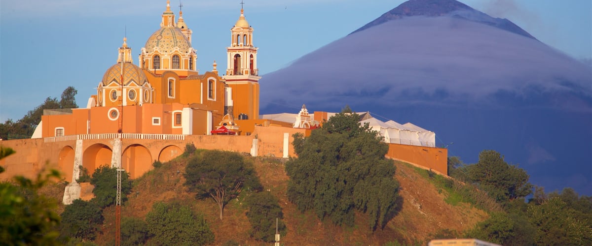 A church with two domes and a bell tower, a mountain in the background, and a red tent on the hill.