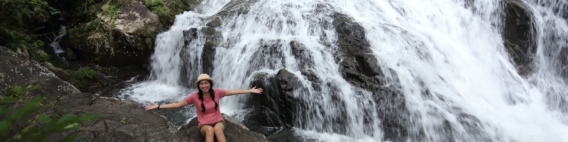 Uma pessoa sentada sobre uma rocha com os braços estendidos à frente de uma cascata.