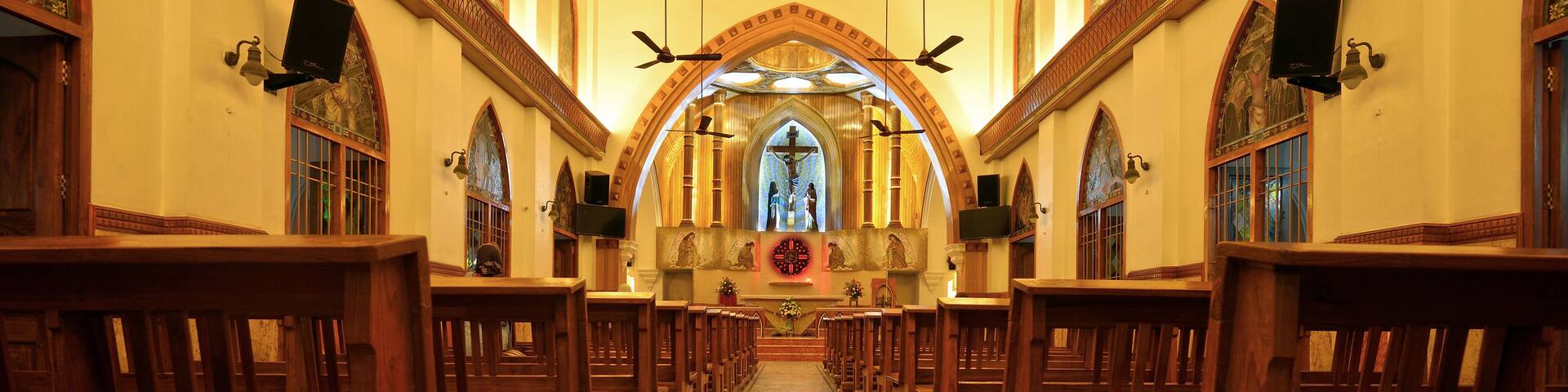 A church interior with wooden pews, a marble floor, and stained glass windows.