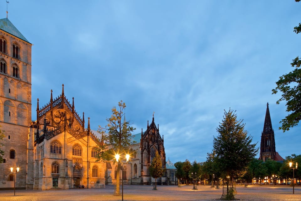 Eine historische Kathedrale mit hohem Turm und filigraner Architektur, umgeben von Bäumen und einem Pflasterplatz.