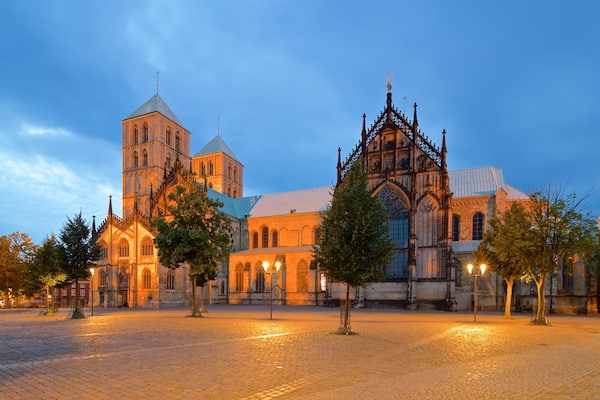 Eine historische Kirche mit gotischer Architektur, darunter spitzbogige Fenster und ein schlanker Turm, vor einem Dämmerhimmel.