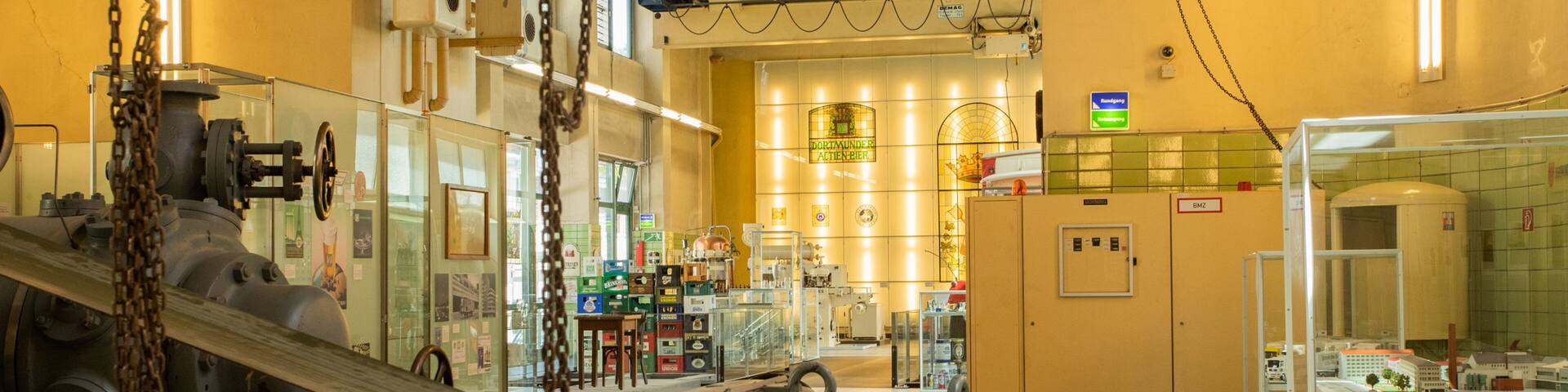 A museum interior with industrial machinery, glass display cases, and a yellow wall with a sign.
