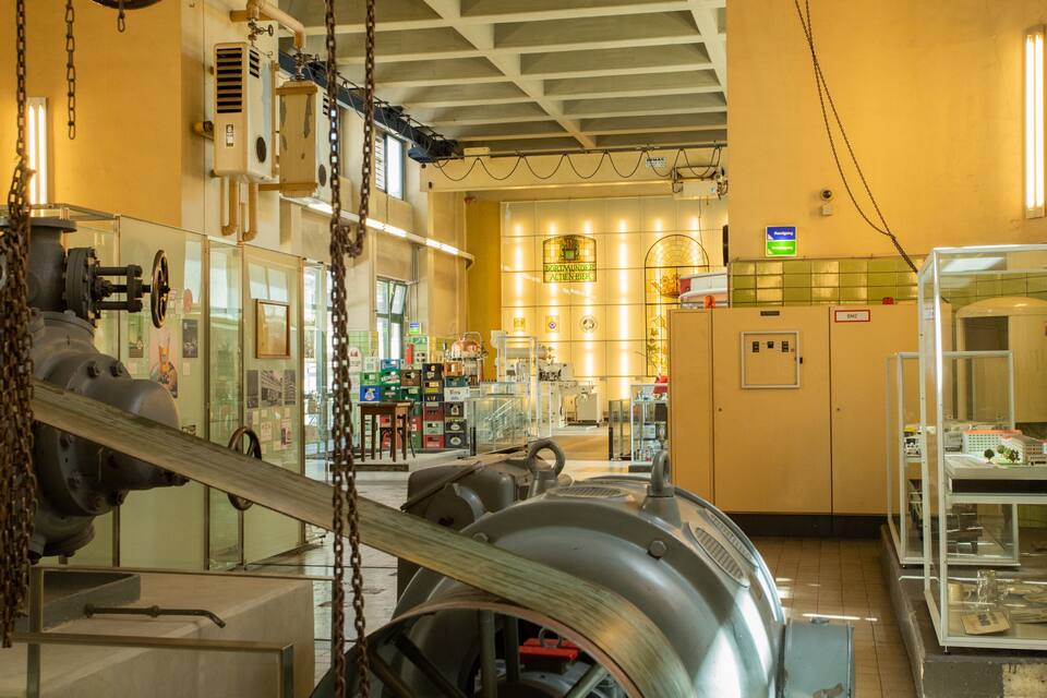 A museum interior with industrial machinery, glass display cases, and a yellow wall with a sign.