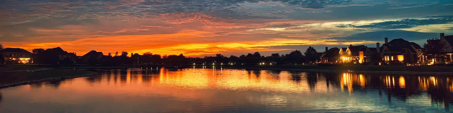 A sunset over a calm lake with reflections of buildings and trees.