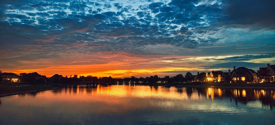 A sunset over a calm lake with reflections of buildings and trees.