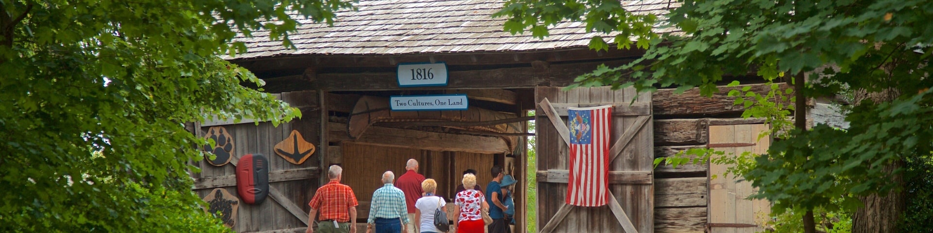 Un edificio de madera con un letrero que dice "1816 Dos Culturas, Una Tierra" y una bandera estadounidense.