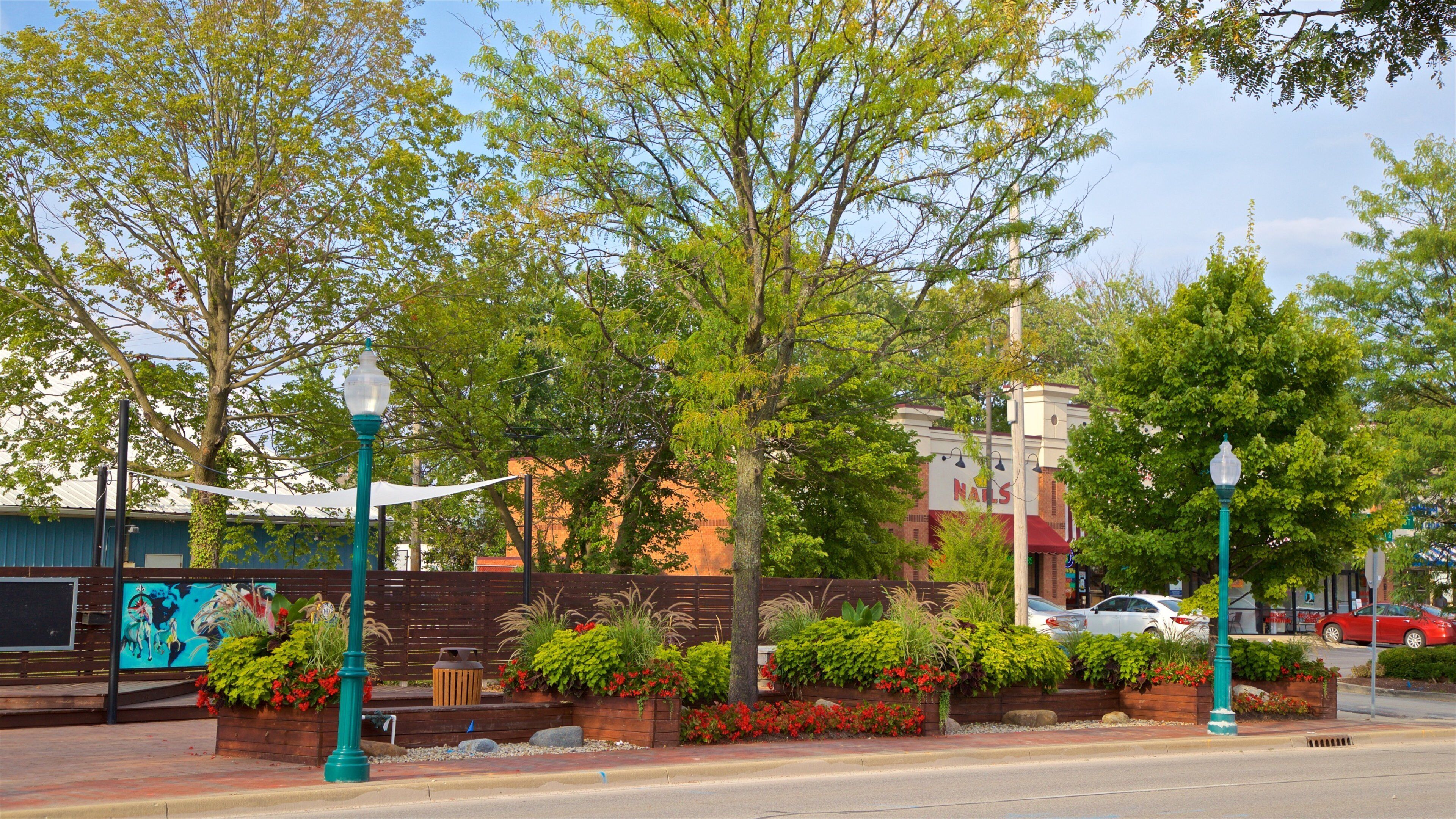 A street with trees, a fence, and a building with a red awning.