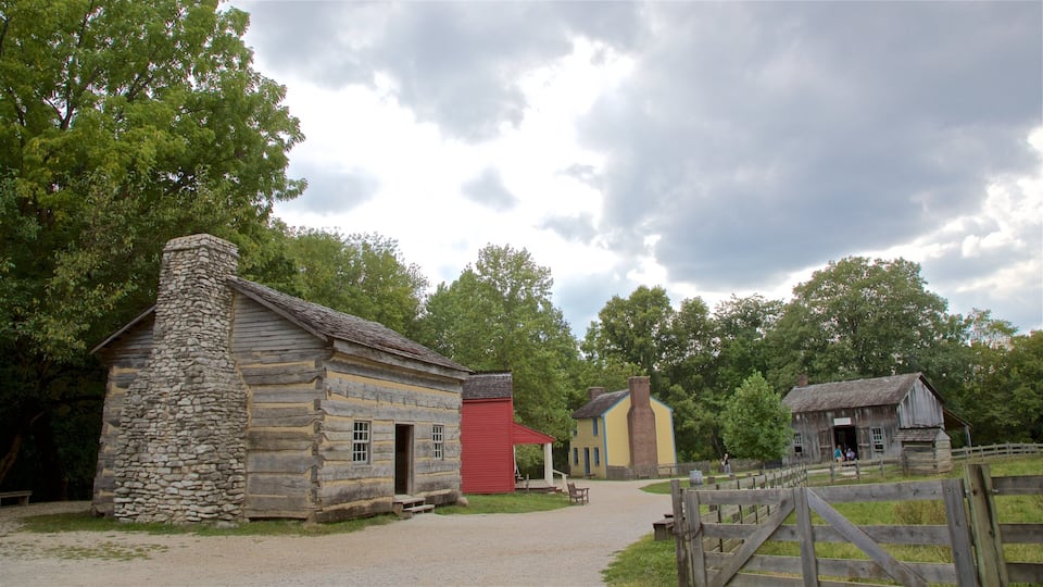 A historic log cabin with a stone chimney, a red building, and a yellow building with a brick chimney.