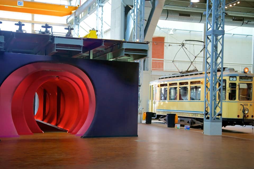 A tram in a museum with a large red tunnel structure.