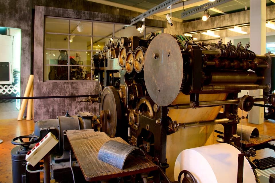 Een oude drukpers met grote tandwielen en rollen, omringd door houten meubels en metalen onderdelen.